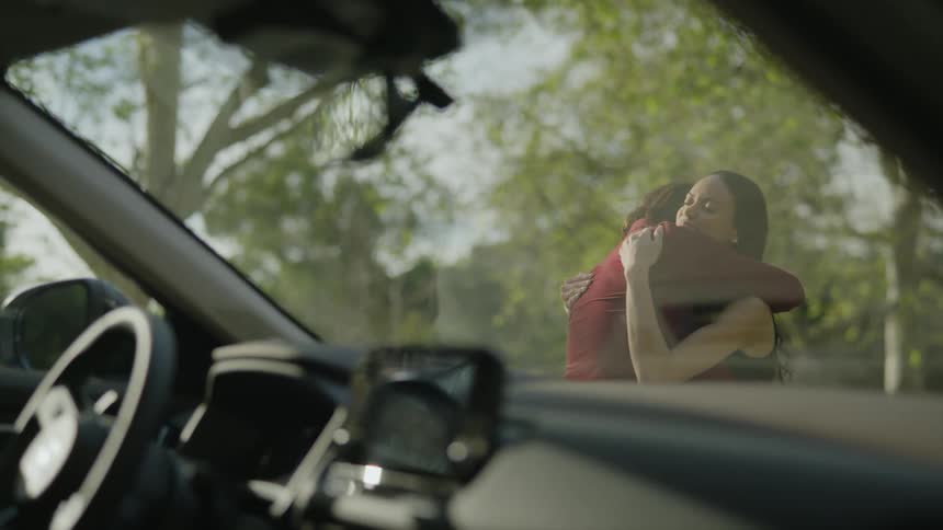A man and woman standing road side smile and talk and give each other a big hug