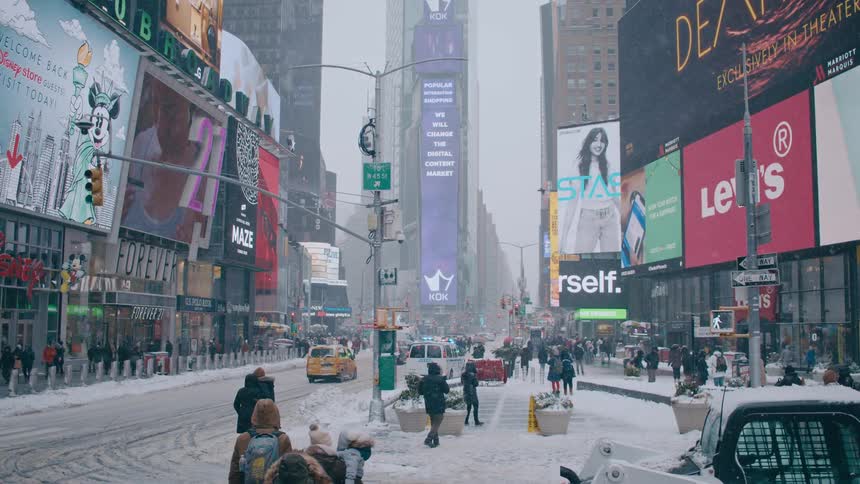 People walk down a city street covered in snow past stores