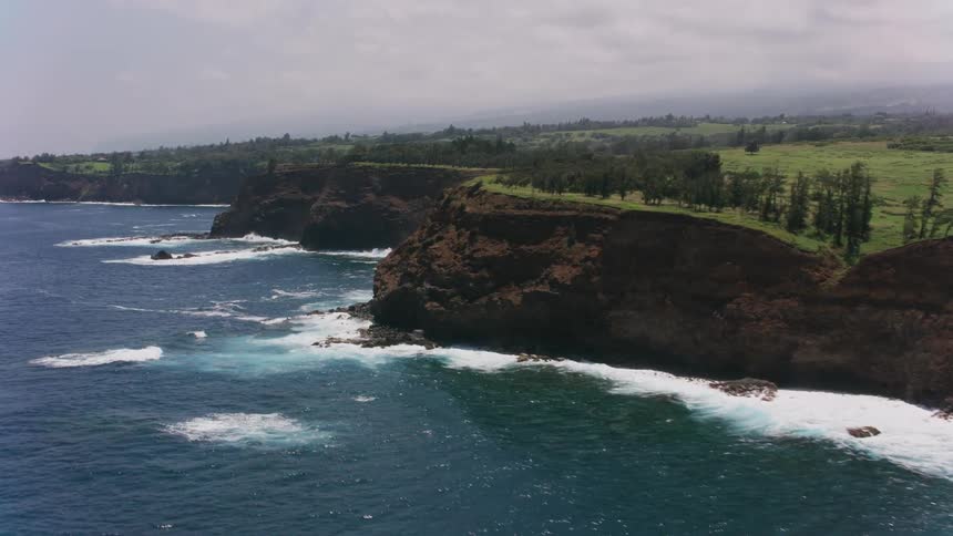Waves roll into shore below the cliffs along the coast under a cloudy sky