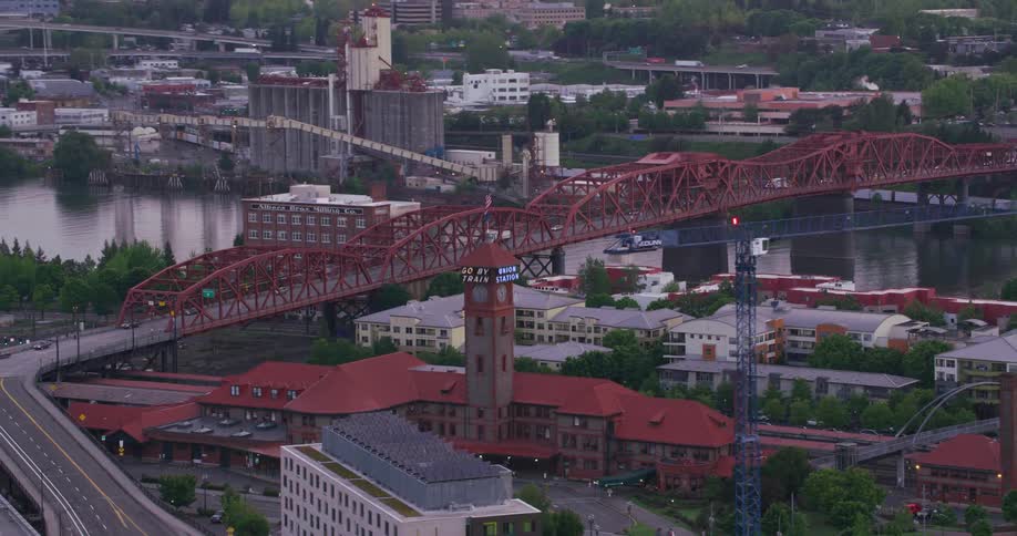 A clock tower sits near a bridge over a river through downtown