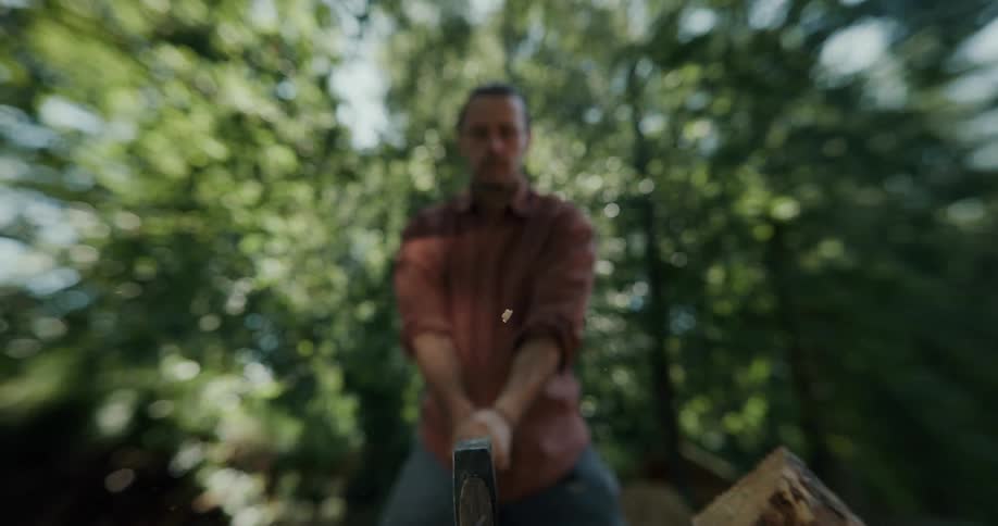 Man chopping a piece of wood with an ax over a stump outodoors