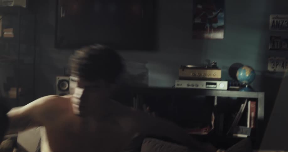 A man retrieves a virtual reality headset from a bookcase before sitting on a sofa and putting the headset on his head