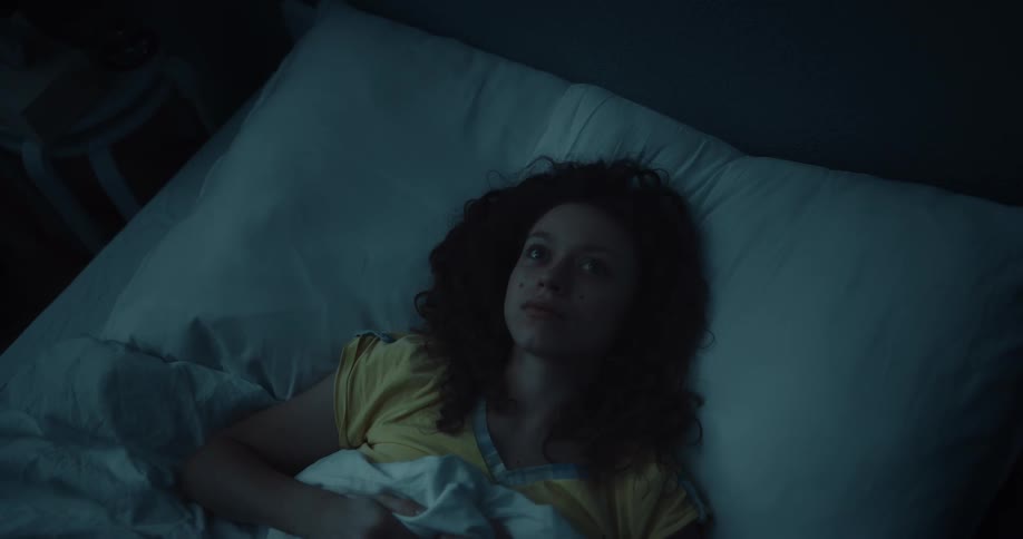 A woman is lying awake in bed as lightning flashes
