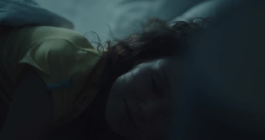 A woman lying in bed stares up at the ceiling before turning to her side and closing her eyes