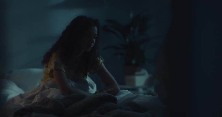 A young woman resting in bed sits up and turns on a lamp before climbing out of bed