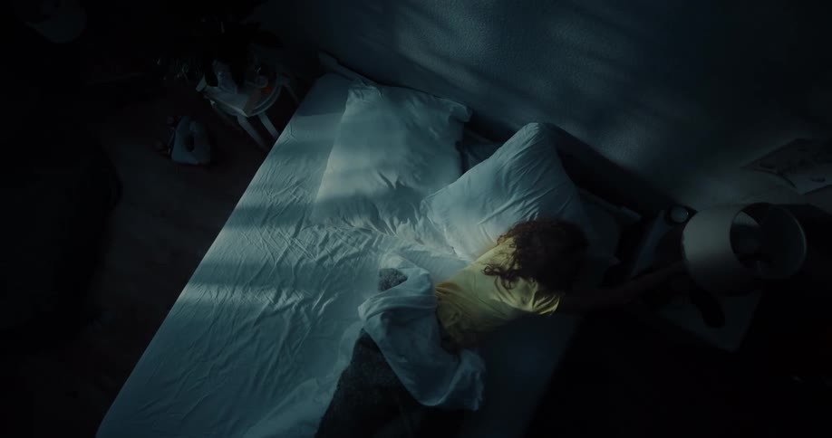 A woman laying in bed suddenly rolls over and turns on the light then gets out of bed