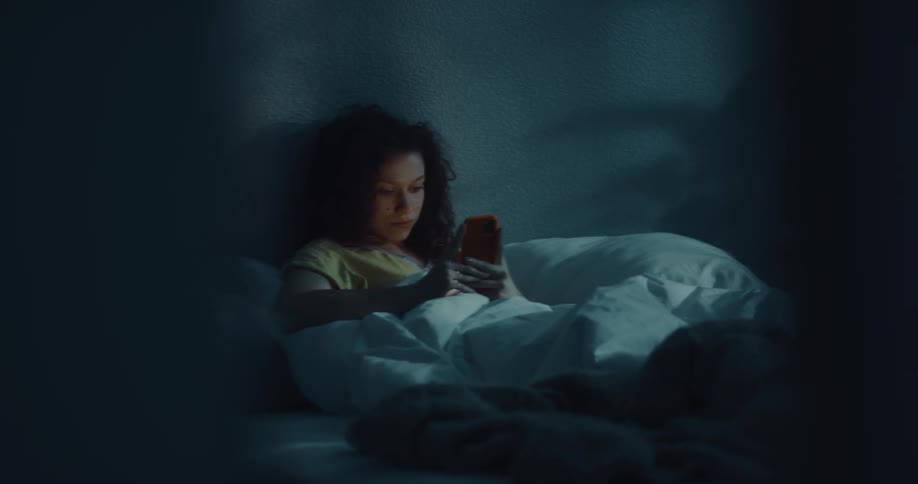 A woman laying in bed sits up and starts looking at her phone