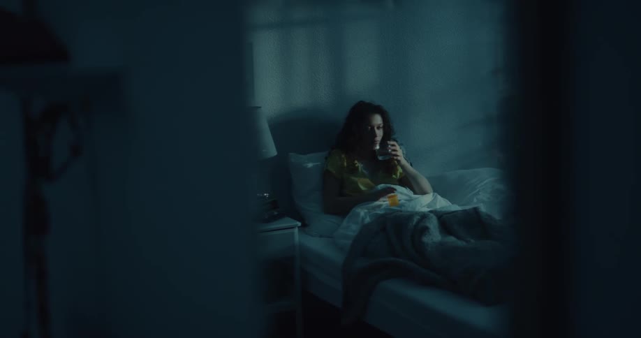 A woman sits up in bed reaches for the pill bottle on her night stand and takes some with water
