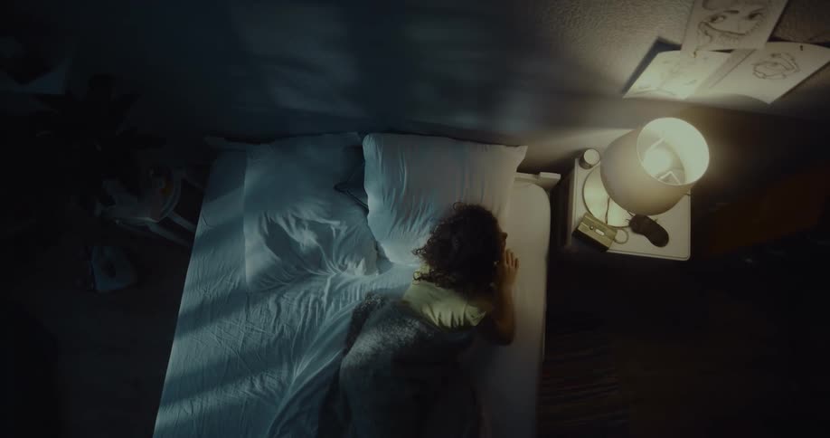 Woman lying on bed sits up and turns on light before using cellphone