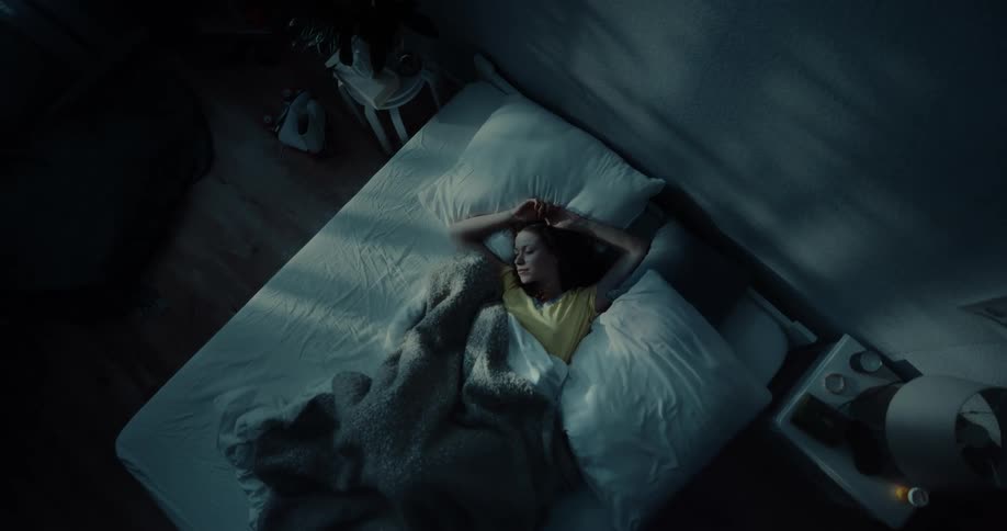 Woman tosses and turns on bed in a dark bedroom