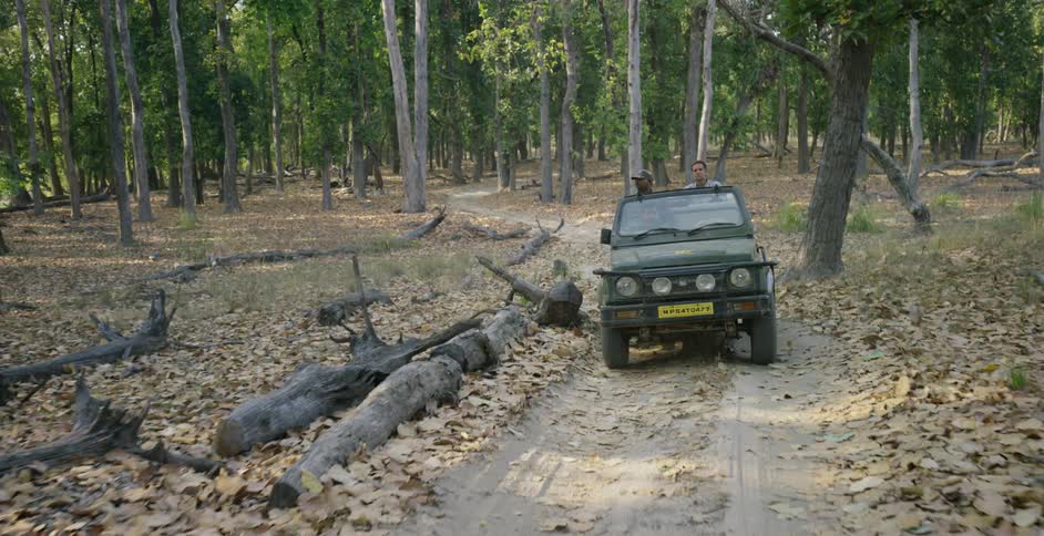 A vehicle rides on a dirt road with two people sitting in it