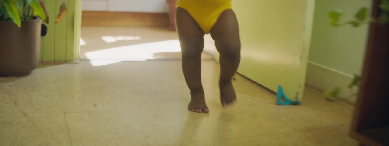 Black toddler girl with yellow clothes walks from room to room at home