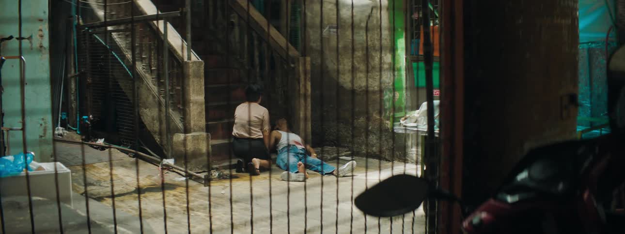 A woman kneeling next to a man laying bleeding at the bottom of a staircase