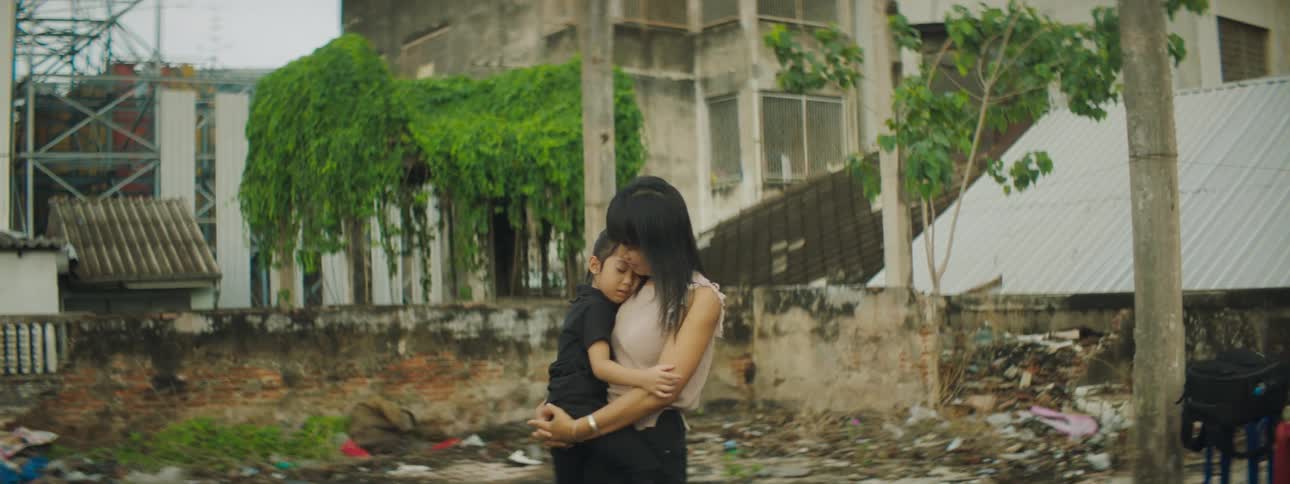 A woman rocks a little girl in her arms while standing in the slums during the day