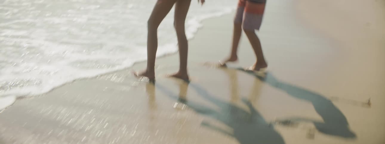 A boy and girl in swimsuits playing in ocean waves on a sandy beach