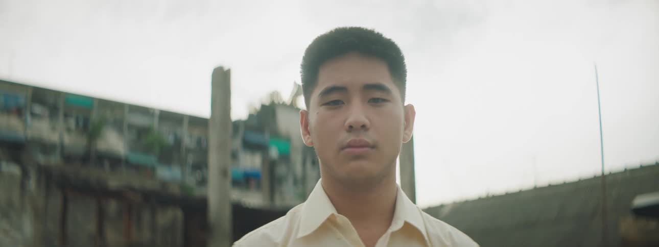 A man standing and staring with buildings the sky and clouds in the background