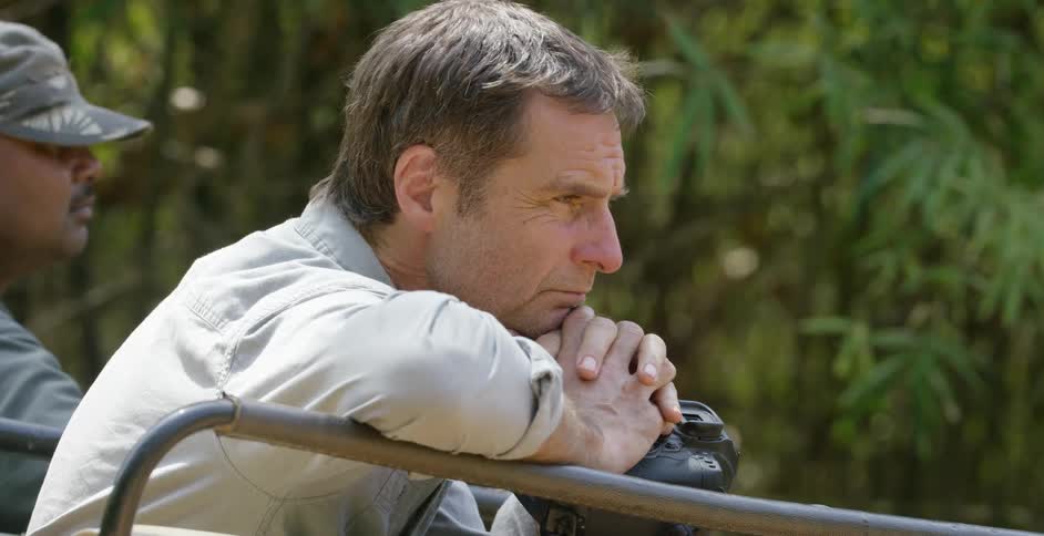 A man holding a camera leans on a metal railing