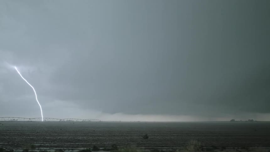 Lightning strikes through dark clouds over a field