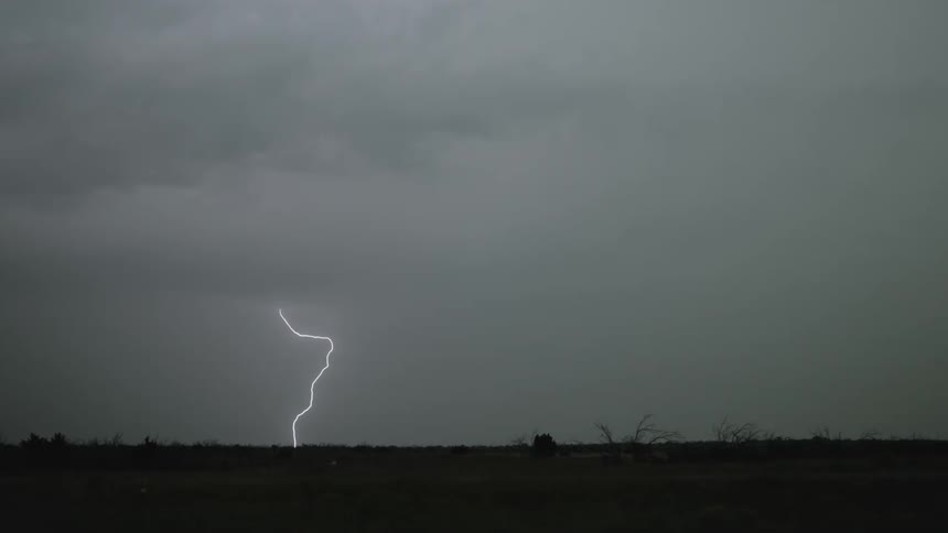 Lightning strikes through dark clouds over a field