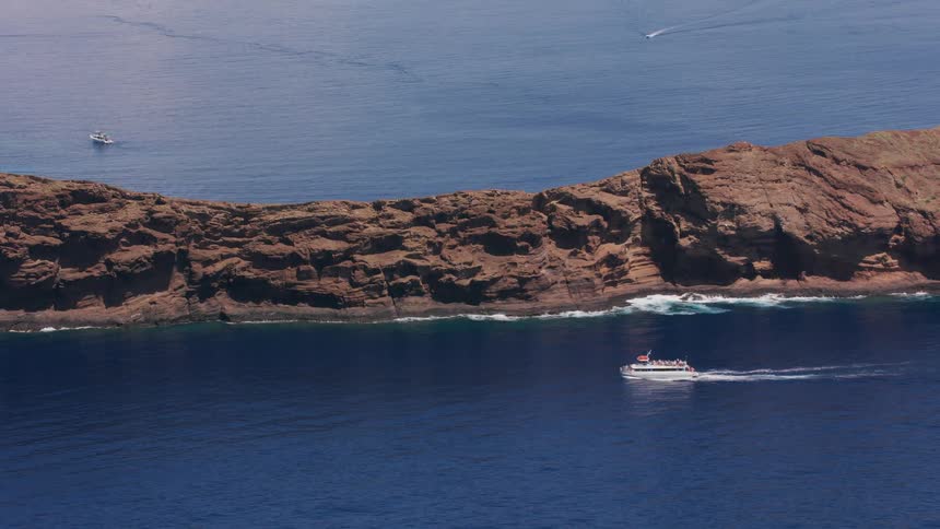 A large boat cruises along the coastline a rocky prominence that protrudes into the ocean