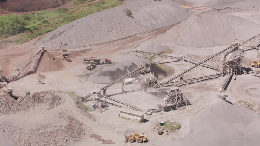 An aerial view of trucks driving across sand at a refinery
