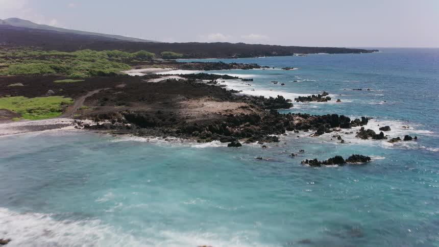 Waves roll into shore crashing against rocks along the coast and there is a mountain in the distance
