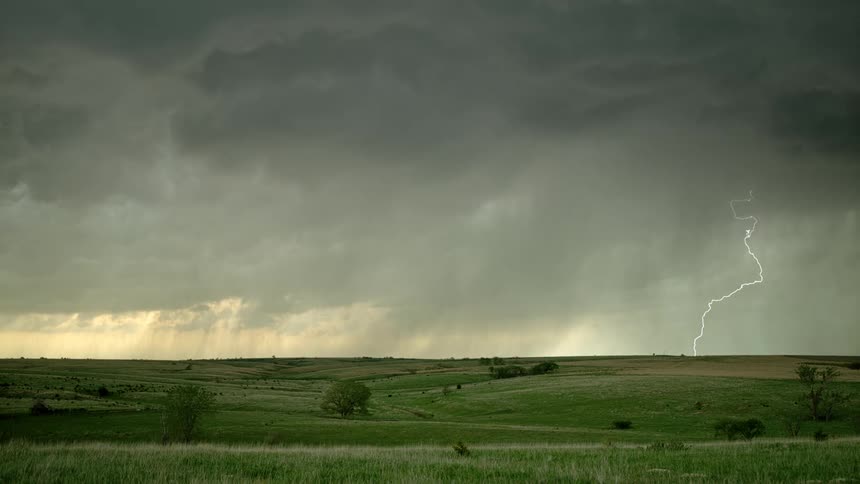 Lightning strikes from huge rain and thunder clouds above green fields