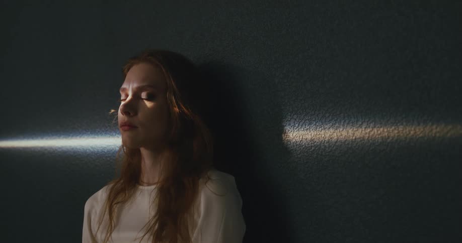 A woman opens her eyes while leaning against a wall