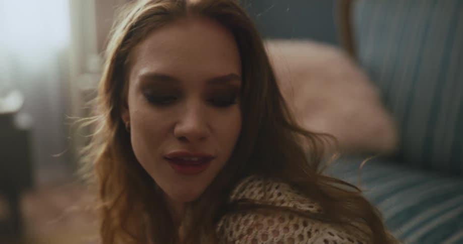 A woman dances and flirts with the camera while sitting on the floor in a living room