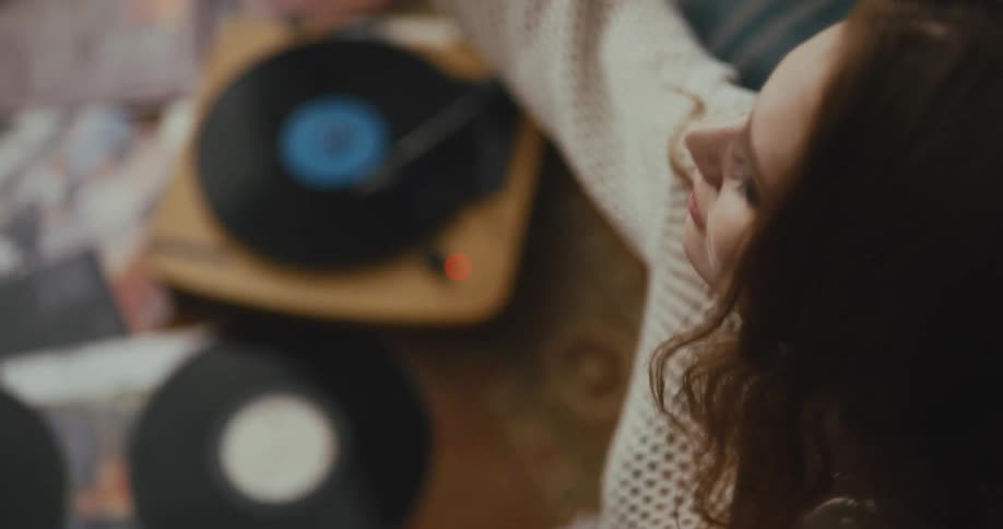 A woman dances and stretches back smiling while sitting listening to record albums