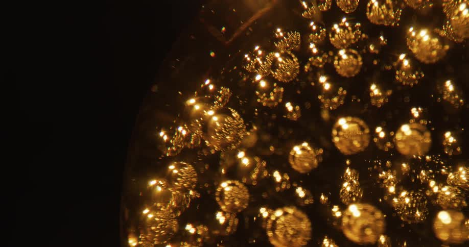 Shiny gold spheres inside a clear globe reflect light as they turn