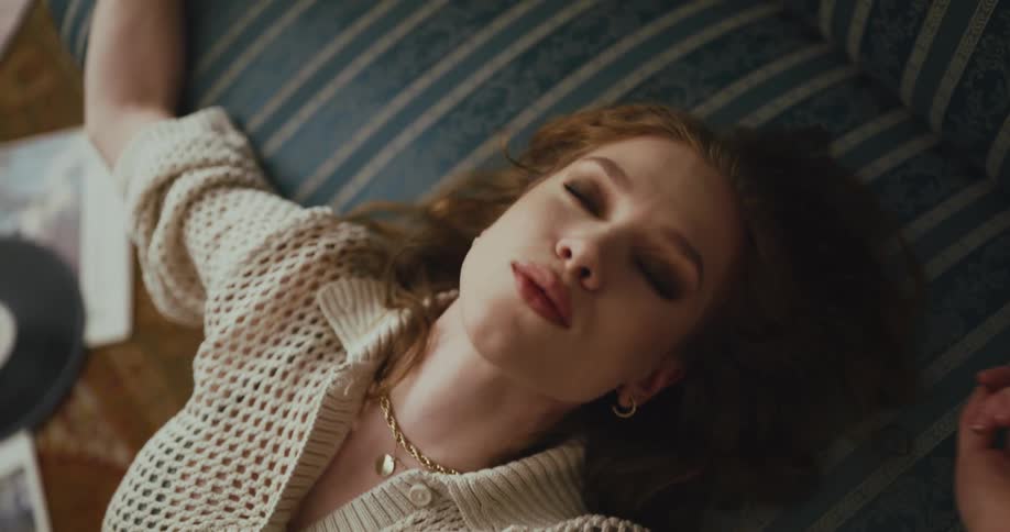 A woman dances while listening to music sitting on the floor leaning back on the couch