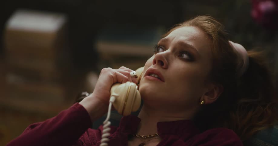 A woman looks very distressed as she speaks to someone on an old style telephone and then lets the receiver rest on her shoulder