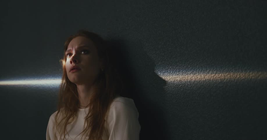 A teenager girl looking sad leans against a wall