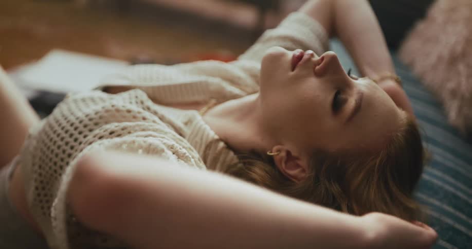 A woman is sitting on the floor against a couch leaning back and putting her hands through her long hair