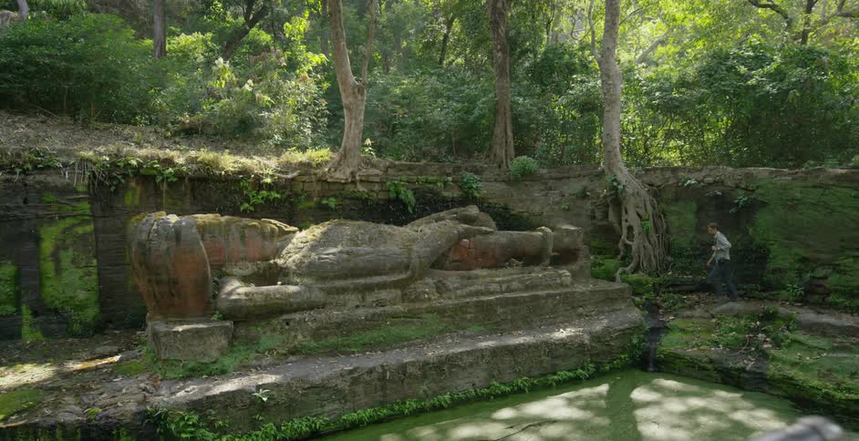 A man hikes past a large statue laying in a pit