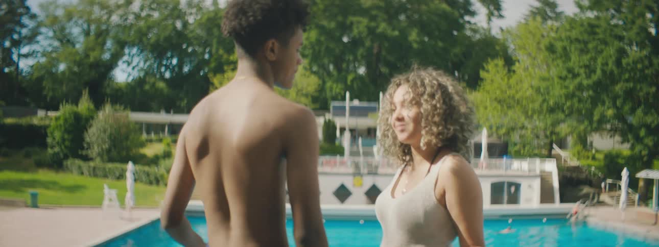 Man walks to woman near large backyard swimming pool and kisses her