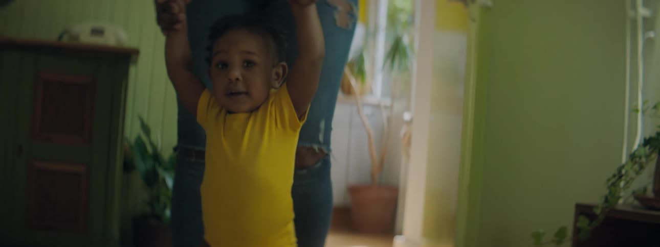 A woman holds the hands of a child to help the child walk through a house during the day