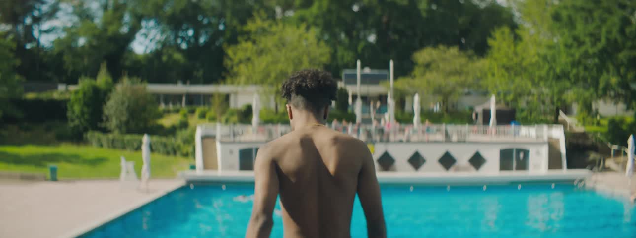 A young man walks up to an outdoor pool and looks at the water