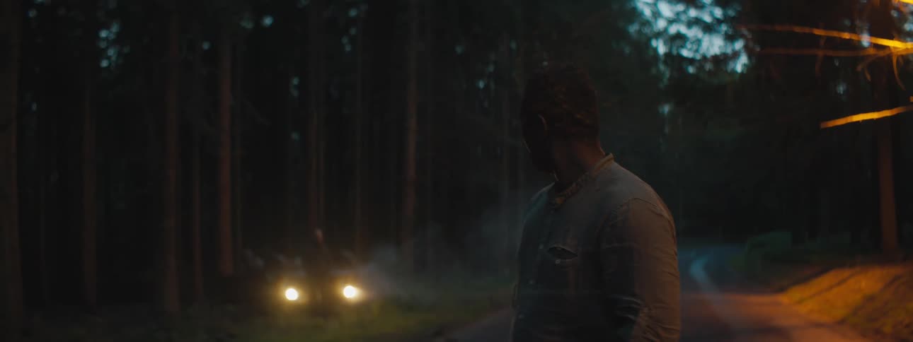 A man turns around and looks as hewalks down a road away from another man who has his car on the shoulder