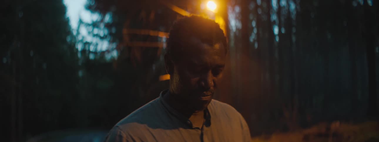 A man is standing in a forest and looking sad
