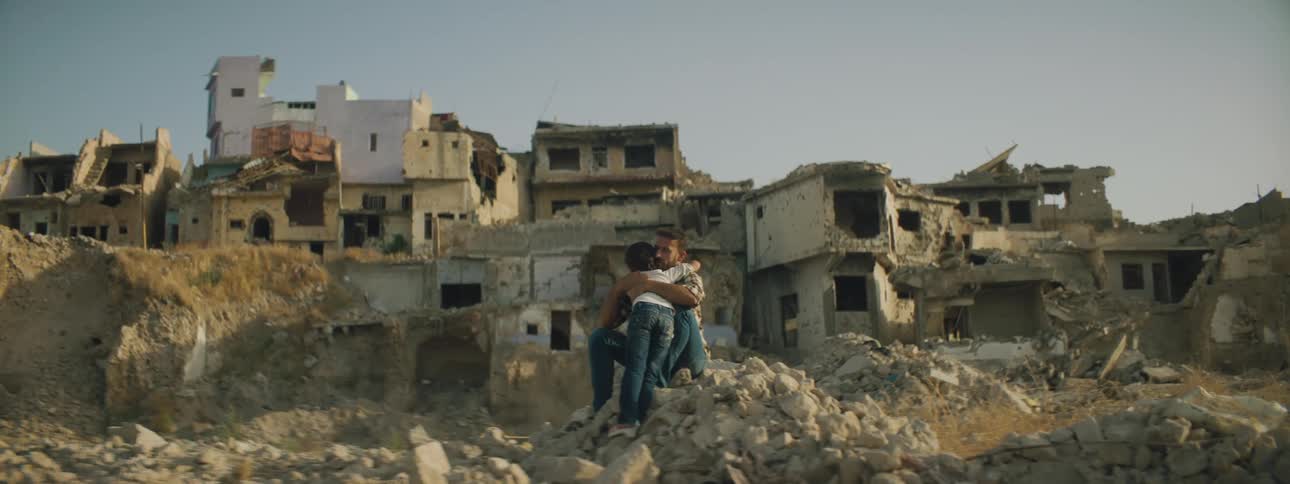 A man hugs two girls in front of buildings that are falling apart