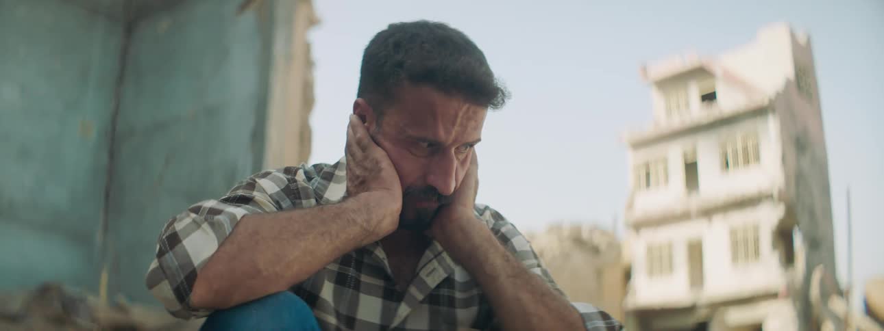 A man sitting with a wall a building the sky and clouds in the background