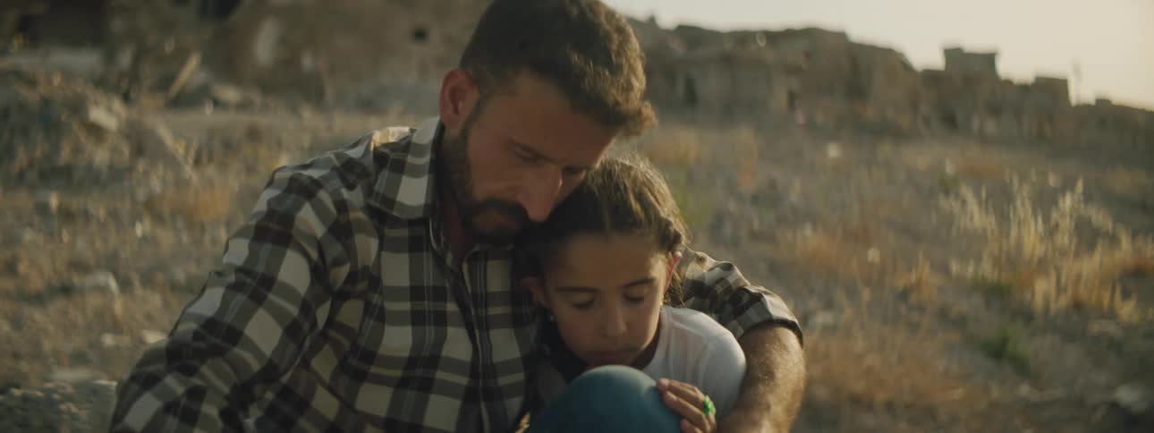 Father and daughter sitting on a barren slope near an abandoned village at sunset