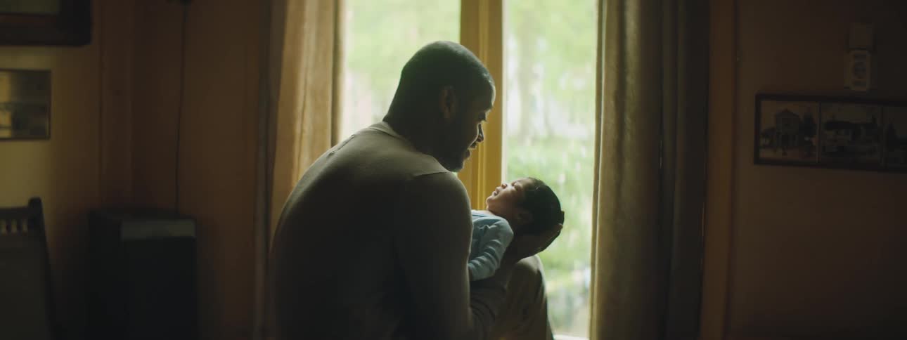 Man holds son talking to him with a smile near window