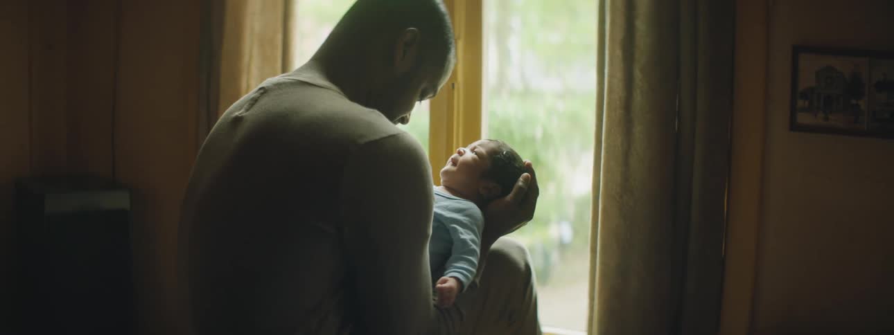 Father with a sweatshirt holds and talks to his baby next to the windows in a room