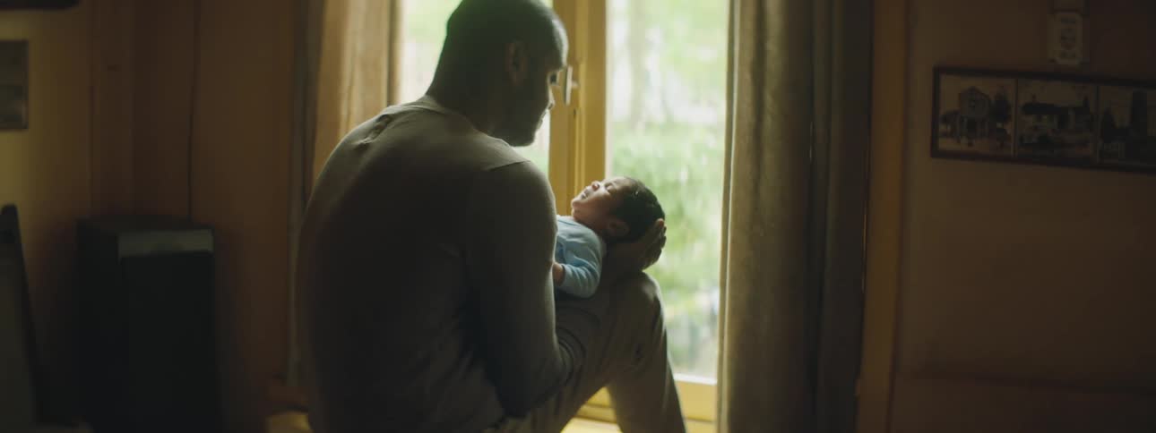 A man sits next to a sunny window holding his infant