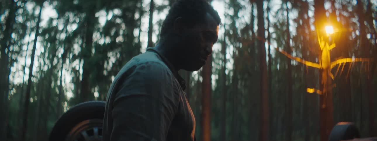 A man standing in the woods near a turned over car