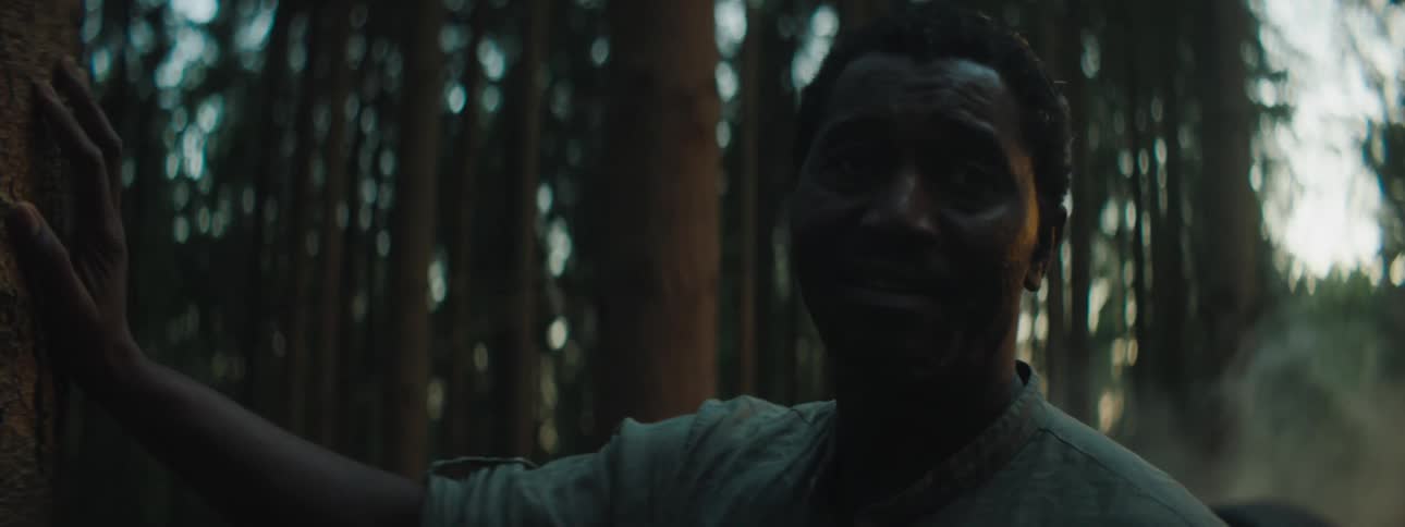 A man standing next to his car which is flipped upside down steadies himself against a tree and looks up and then wraps his arms around his chest