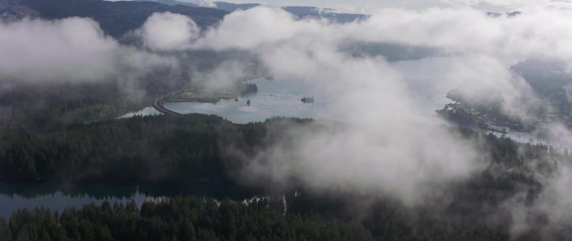 An aerial view of clouds covering a forest and lake